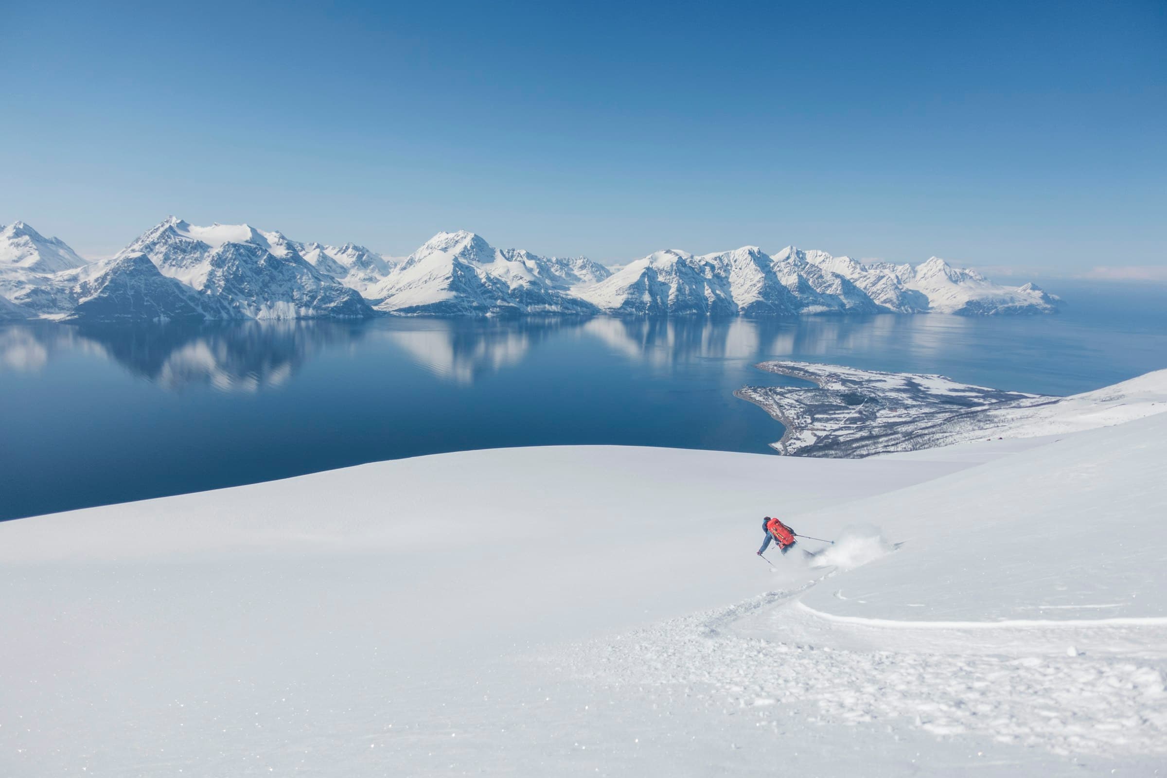 Lone skier making fresh tracks on a vast snowfield above a fjord
