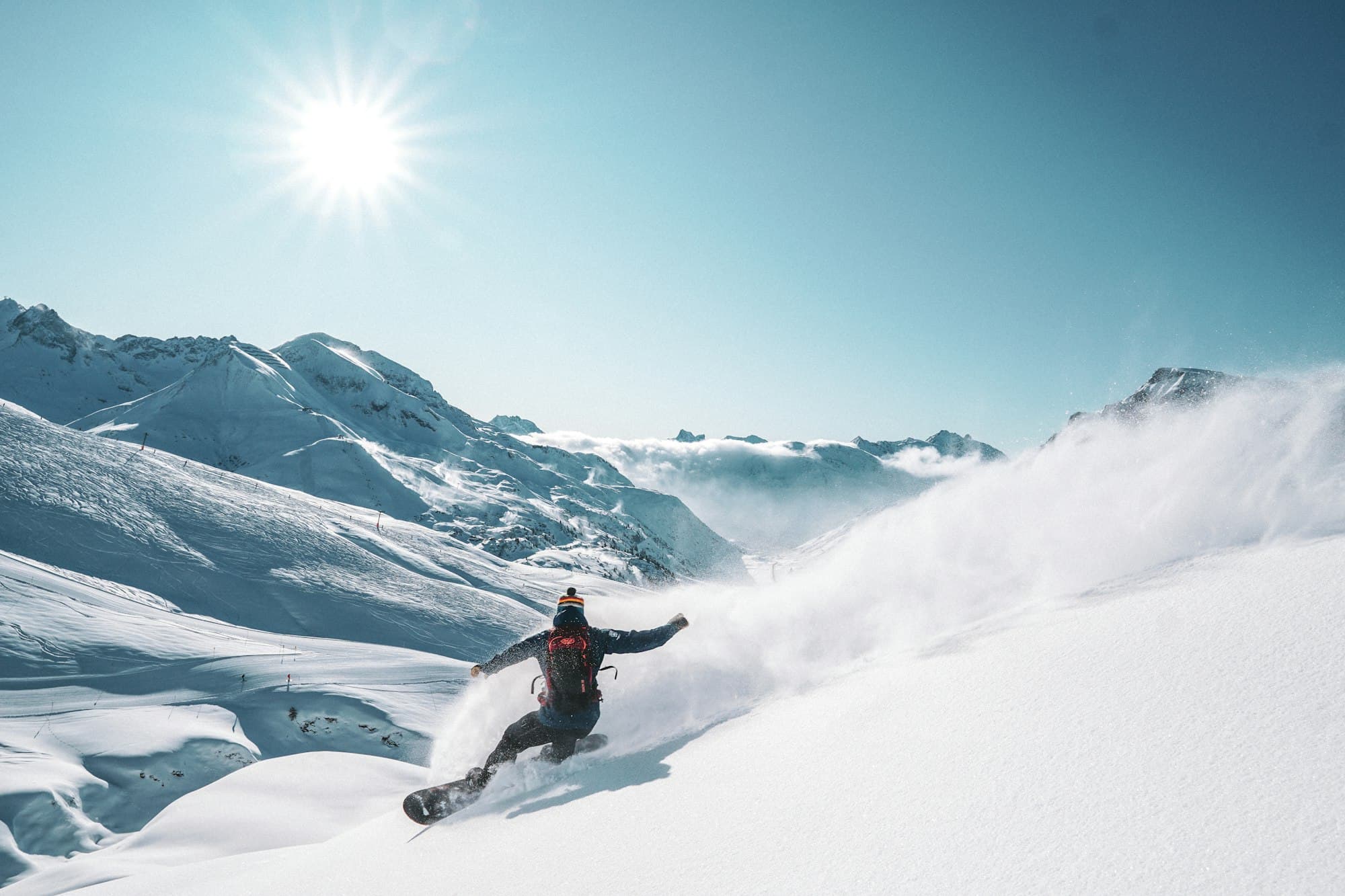 Snowboarder carving through powder under a bright sun